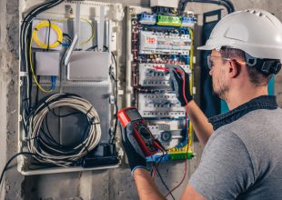 Man, an electrical technician working in a switchboard with fuses. Installation and connection of electrical equipment. Professional uses a tablet.