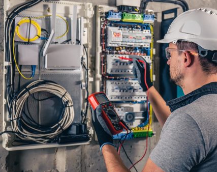 Man, an electrical technician working in a switchboard with fuses. Installation and connection of electrical equipment. Professional uses a tablet.